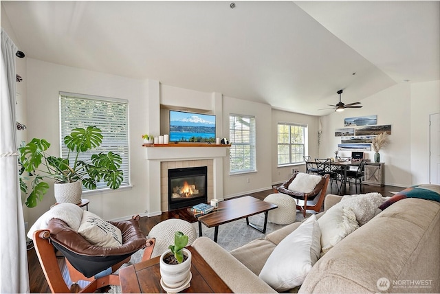 living area featuring wood finished floors, baseboards, ceiling fan, a tiled fireplace, and vaulted ceiling