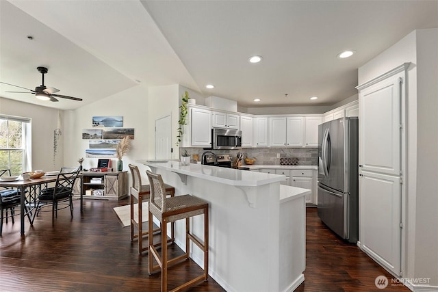 kitchen featuring a breakfast bar area, backsplash, white cabinets, a peninsula, and stainless steel appliances