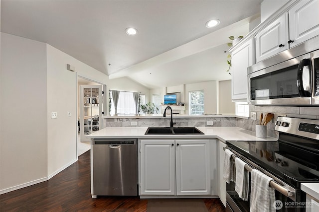 kitchen with a peninsula, dark wood-style floors, a sink, appliances with stainless steel finishes, and vaulted ceiling