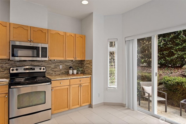kitchen featuring baseboards, light tile patterned floors, backsplash, and stainless steel appliances