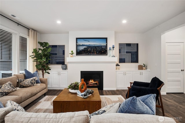 living area featuring recessed lighting, baseboards, a glass covered fireplace, and dark wood-style floors