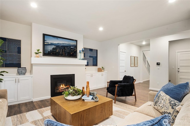 living room with a glass covered fireplace, wood finished floors, baseboards, stairway, and recessed lighting