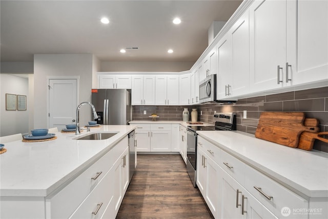 kitchen featuring appliances with stainless steel finishes, a sink, white cabinetry, decorative backsplash, and visible vents