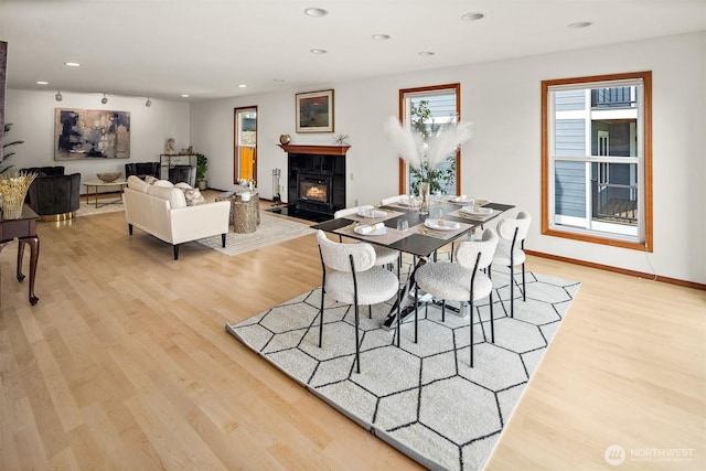 dining space with light wood-type flooring, a tiled fireplace, recessed lighting, and baseboards
