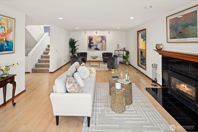 living area featuring light wood-style floors, a tile fireplace, stairway, recessed lighting, and baseboards