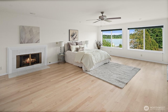 bedroom with wood finished floors, a tile fireplace, baseboards, and ceiling fan