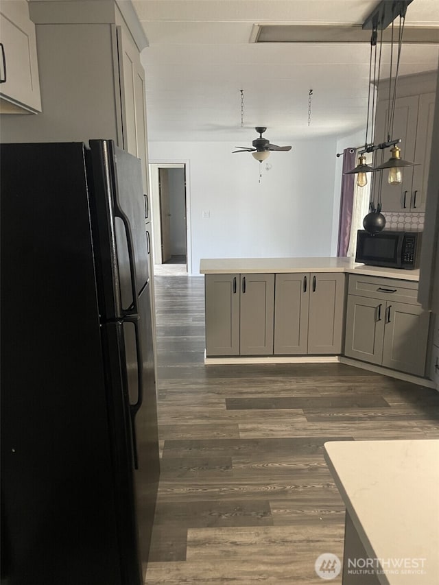 kitchen with dark wood-style flooring, a peninsula, light countertops, gray cabinets, and black appliances