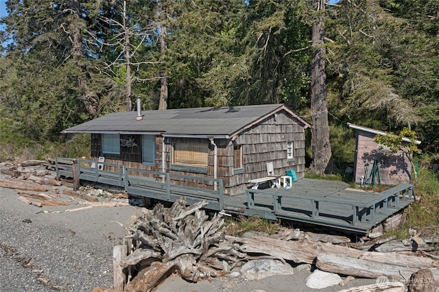 view of front of house featuring a wooden deck, an outbuilding, a shed, and a forest view