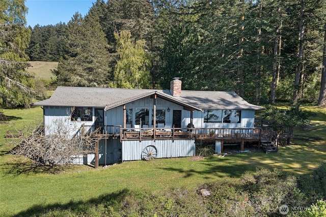 back of property featuring a lawn, a view of trees, a wooden deck, and a chimney