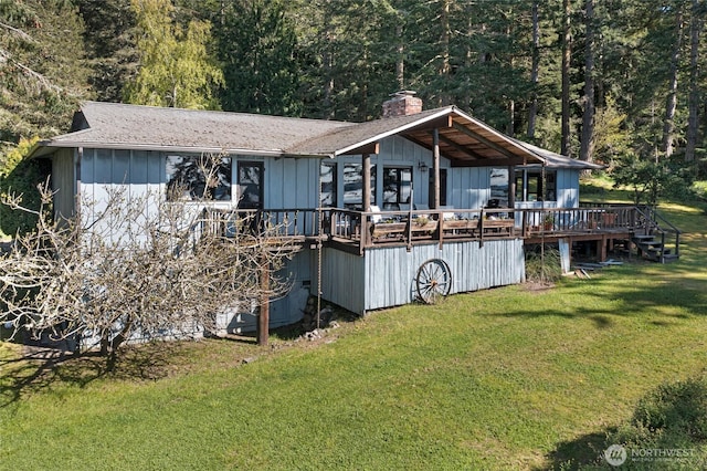back of property featuring a lawn, a forest view, a chimney, and a wooden deck