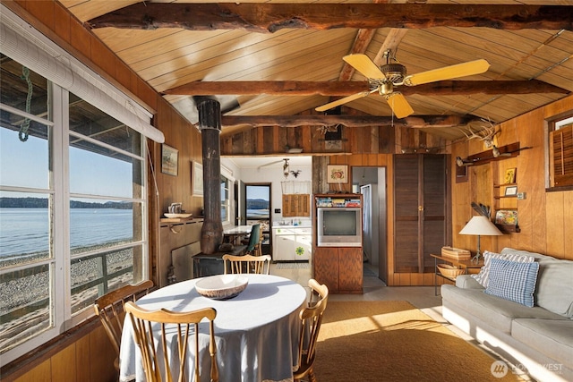 dining area featuring a ceiling fan, wood walls, vaulted ceiling with beams, and a water view