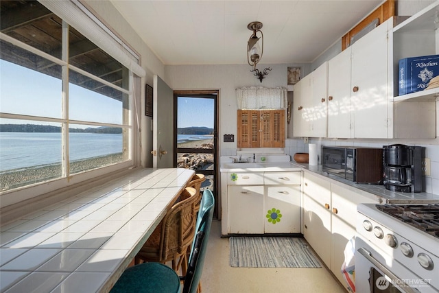 kitchen with white cabinets, black microwave, gas range gas stove, decorative backsplash, and a water view