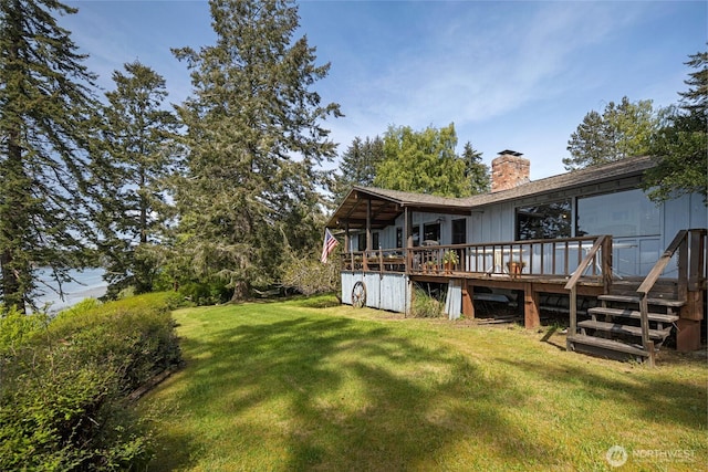rear view of property featuring a wooden deck, a chimney, and a yard