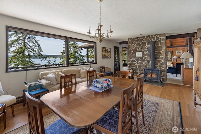 dining room featuring a wood stove, light wood-type flooring, a textured ceiling, and a chandelier