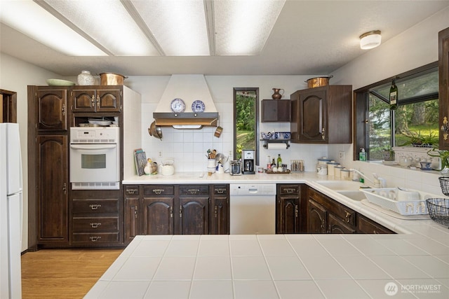 kitchen with dark brown cabinetry, custom exhaust hood, and white appliances