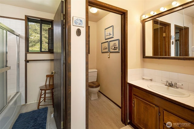 full bathroom with vanity, shower / bath combination with glass door, toilet, baseboards, and tasteful backsplash