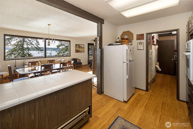 kitchen with freestanding refrigerator, a wealth of natural light, light wood-style floors, tile counters, and a notable chandelier