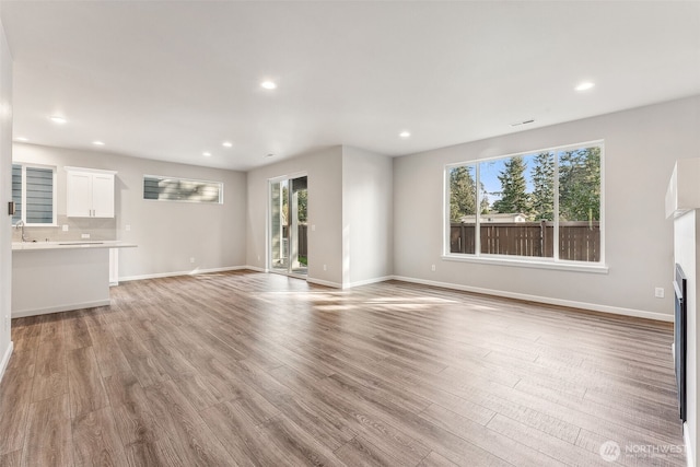 unfurnished living room featuring recessed lighting, a sink, light wood-style flooring, and baseboards