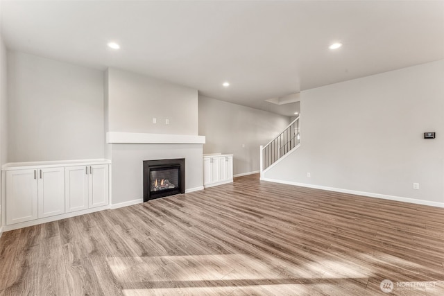 unfurnished living room with recessed lighting, a glass covered fireplace, wood finished floors, and stairway