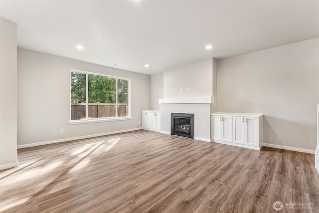unfurnished living room with recessed lighting, baseboards, a glass covered fireplace, and light wood-style floors