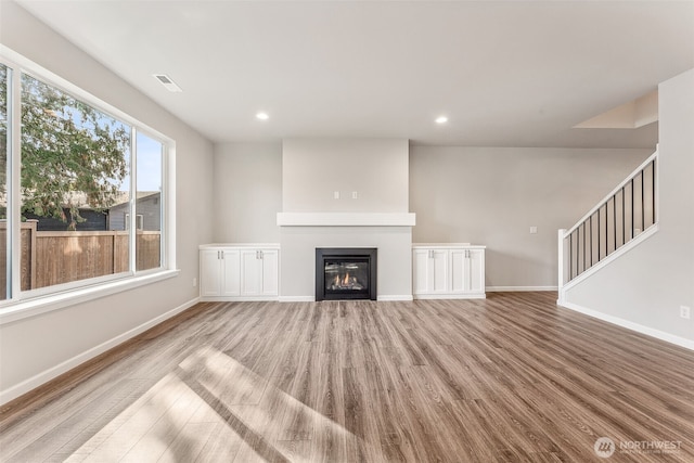 unfurnished living room featuring baseboards, a glass covered fireplace, and wood finished floors