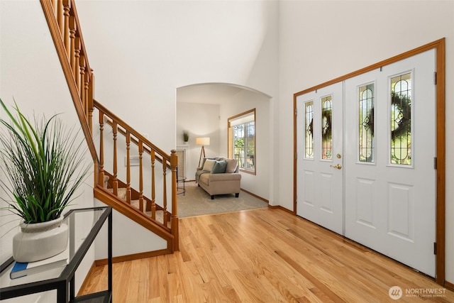 entryway with arched walkways, wood finished floors, stairs, a towering ceiling, and baseboards