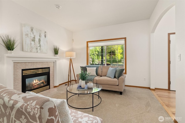 living area featuring a tiled fireplace, baseboards, carpet floors, and arched walkways