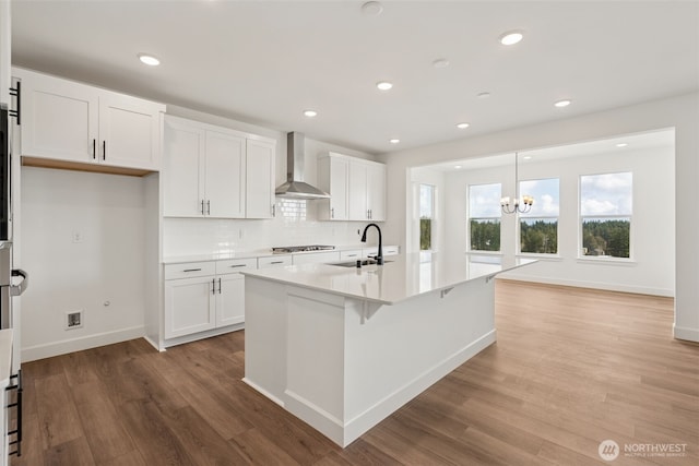 kitchen featuring a sink, white cabinets, light wood finished floors, an inviting chandelier, and wall chimney exhaust hood