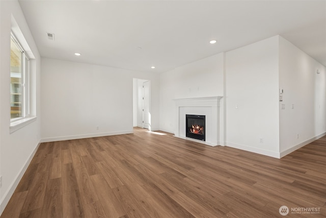 unfurnished living room with a glass covered fireplace, recessed lighting, baseboards, wood finished floors, and visible vents