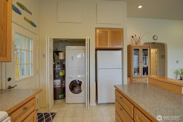 kitchen featuring stacked washer and dryer, water heater, freestanding refrigerator, light tile patterned floors, and visible vents