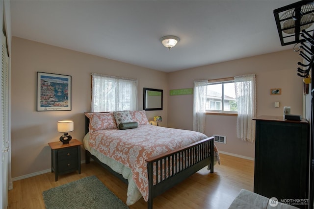 bedroom with baseboards, light wood finished floors, and visible vents