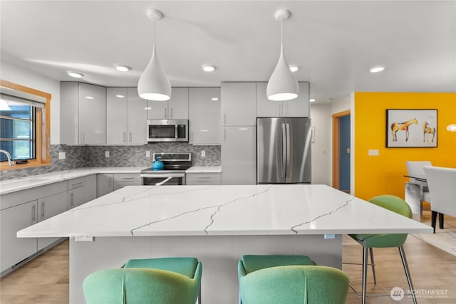 kitchen with gray cabinetry, a breakfast bar, a sink, light wood-style floors, and appliances with stainless steel finishes