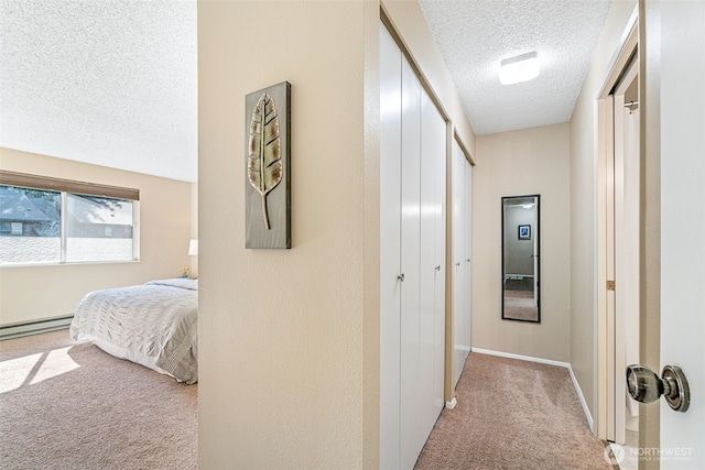hallway featuring light carpet, a textured ceiling, a baseboard heating unit, and baseboards