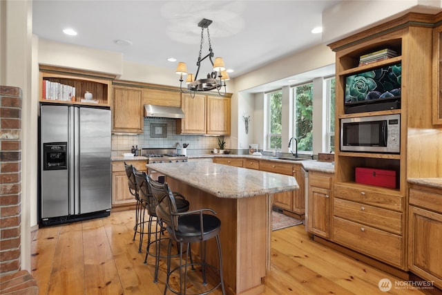 kitchen featuring stainless steel appliances, open shelves, a sink, wall chimney range hood, and light wood-style floors
