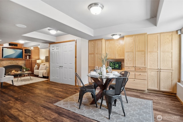 dining space with a raised ceiling, dark wood-type flooring, a lit fireplace, and baseboards