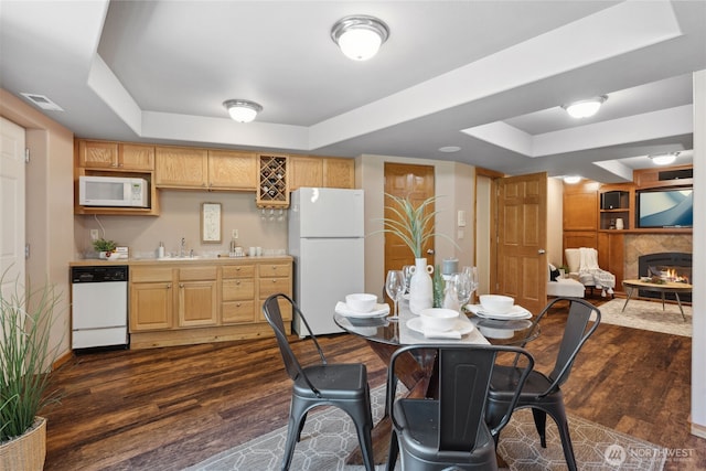 dining room featuring a tray ceiling, wet bar, dark wood-style floors, and a lit fireplace