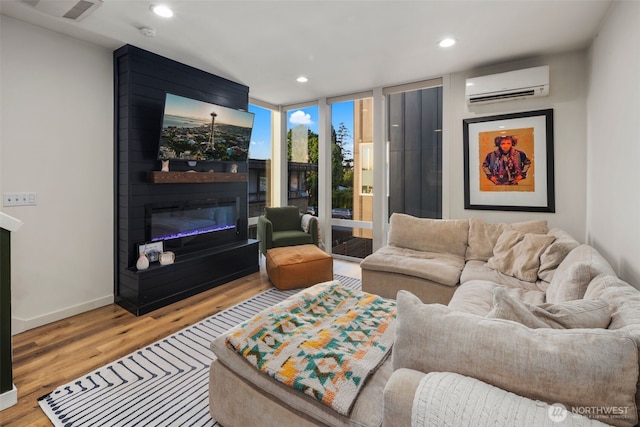 9429 18th Ave SW Unit A, Seattle, WA 98106 - living room featuring a wall mounted AC, a glass covered fireplace, wood finished floors, expansive windows, and recessed lighting