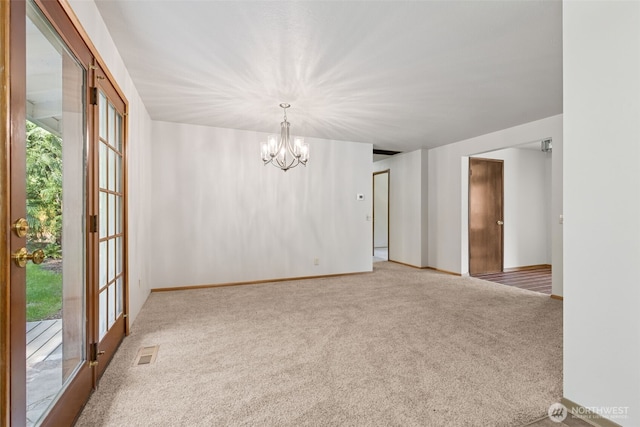 carpeted empty room featuring visible vents, baseboards, and a notable chandelier