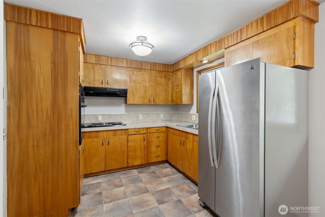 kitchen featuring freestanding refrigerator, stone finish floor, range hood, light countertops, and black cooktop