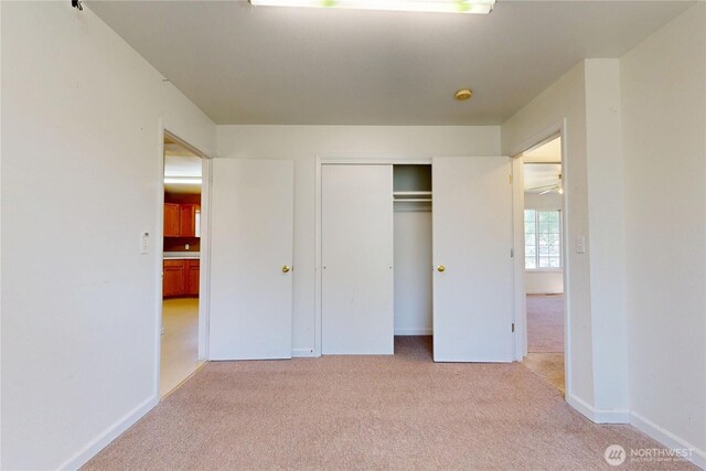 unfurnished bedroom featuring light carpet, a closet, and baseboards