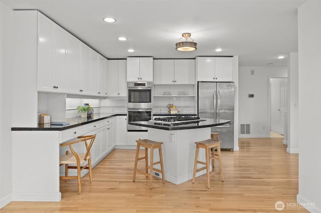 kitchen featuring appliances with stainless steel finishes, baseboards, a breakfast bar area, and light wood finished floors