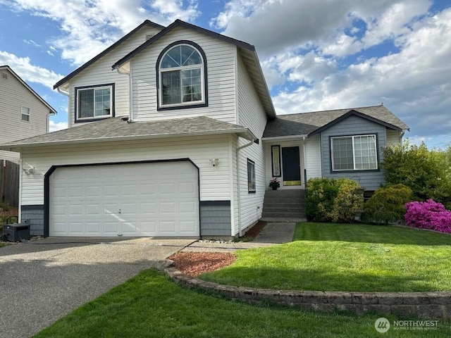 split level home featuring a garage, driveway, roof with shingles, and a front yard