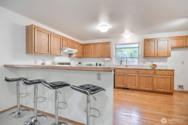1742 N 122nd St, Seattle, WA 98133 - kitchen featuring a breakfast bar, under cabinet range hood, a sink, light countertops, and a peninsula