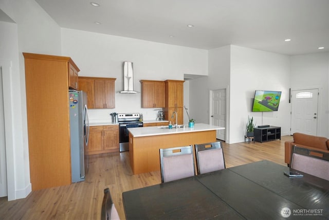 kitchen with wall chimney range hood, appliances with stainless steel finishes, a sink, light countertops, and light wood-style floors