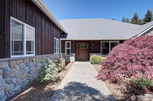 doorway to property featuring stone siding, a shingled roof, and covered porch
