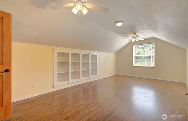 bonus room featuring wood finished floors, a textured ceiling, vaulted ceiling, a ceiling fan, and baseboards