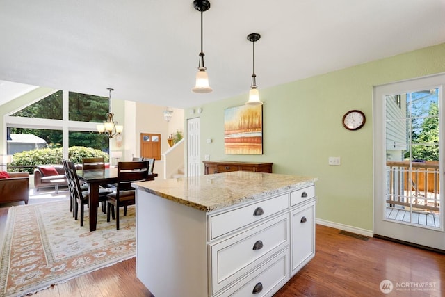 kitchen featuring wood finished floors, light stone countertops, a kitchen island, white cabinets, and a chandelier