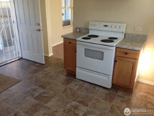 kitchen with white electric range, baseboards, light countertops, and brown cabinets