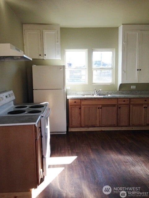 kitchen with a sink, white appliances, brown cabinets, dark wood finished floors, and under cabinet range hood