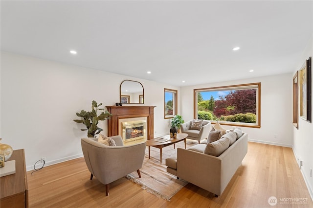 living room with light wood finished floors, a glass covered fireplace, recessed lighting, and baseboards